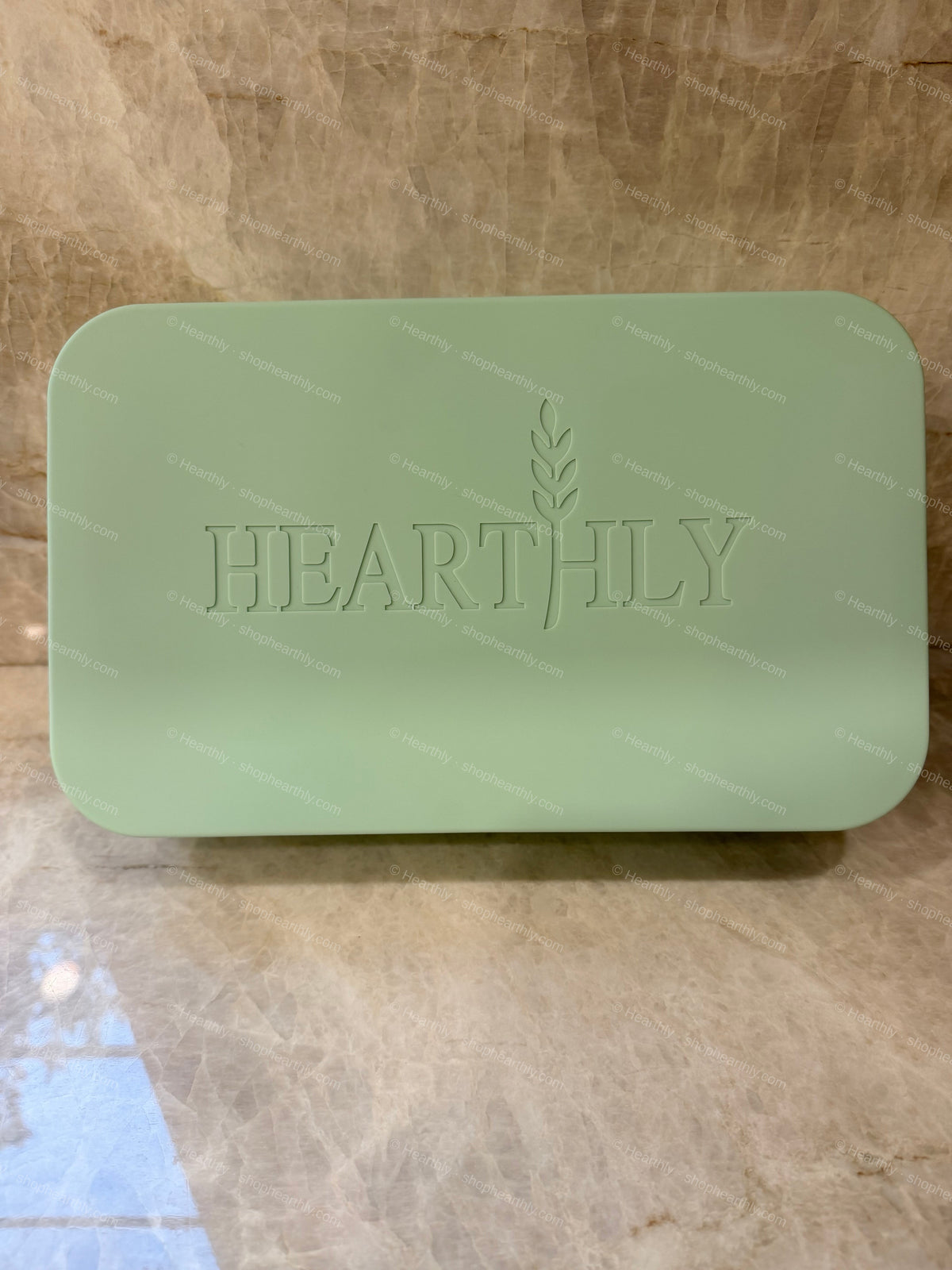 A light green rectangular bar of soap with rounded corners and the brand name 'HEARTHILY' embossed on the front, resting on a beige marble surface.